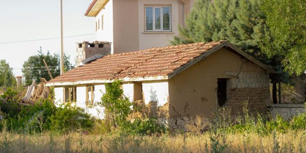 pexels-photo-12949114-12949114 Sunlit abandoned cottage near rural house, depicting rustic charm and decay.